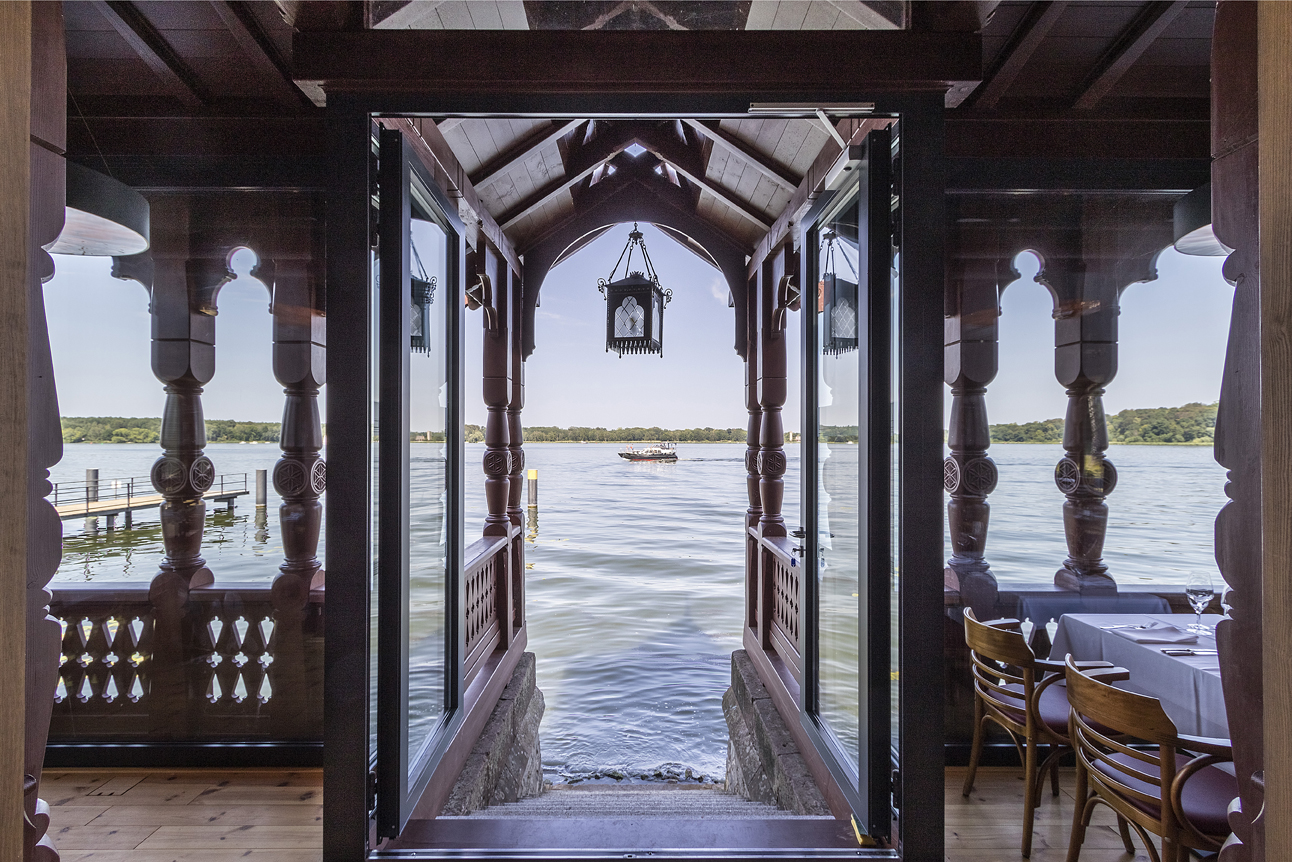 Überdachter Eingang mit Holzsäulen, dekorativen Bögen und Blick auf den See.