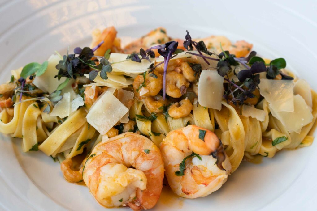 Pasta- oder Gemüsegericht mit Meeresfrüchten, Pilzen und Kräutern auf einem weißen Teller.