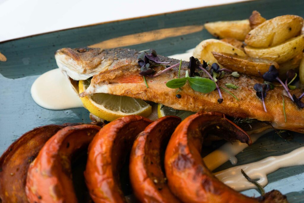 Gegrillter Fisch mit Beilagen, Kräutern und Sauce auf einem rechteckigen Teller.