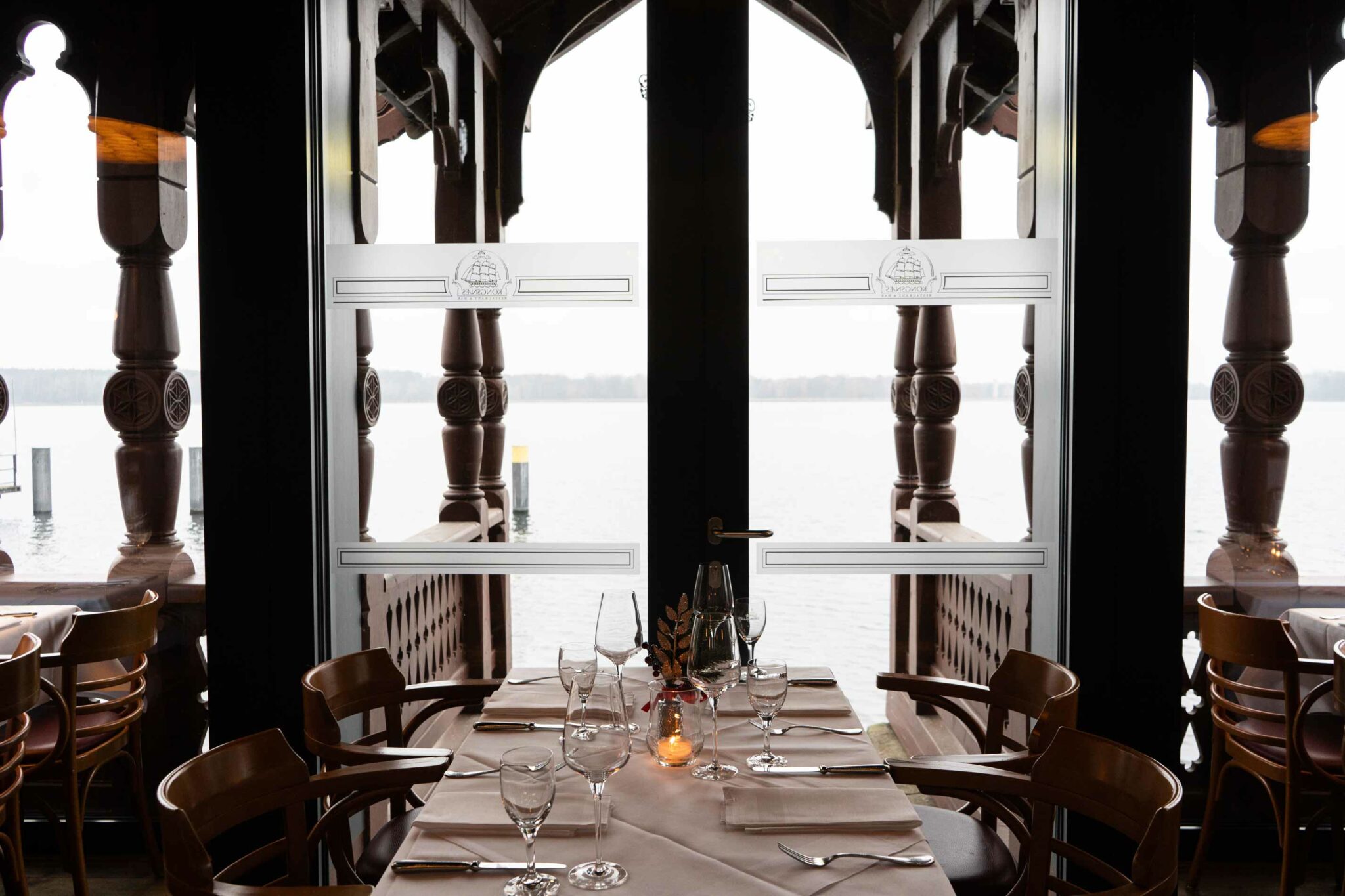 Heller Restaurantbereich mit Holzbalken, gedeckten Tischen und Blick nach draußen.