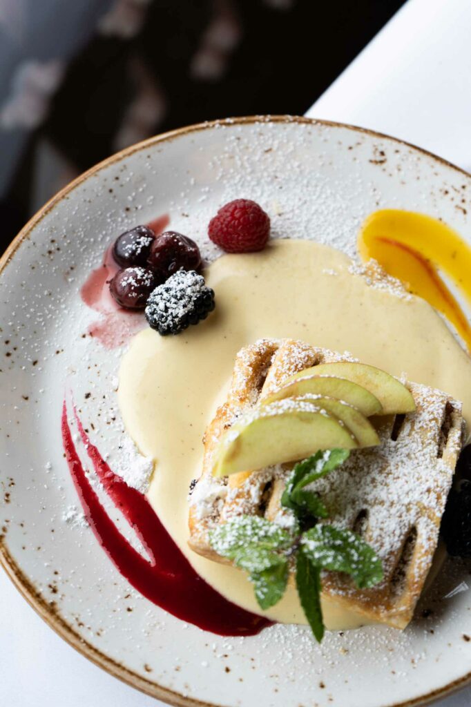 Dessertvariation mit Eis, Früchten, Gebäck und Beerensauce auf einem Teller.