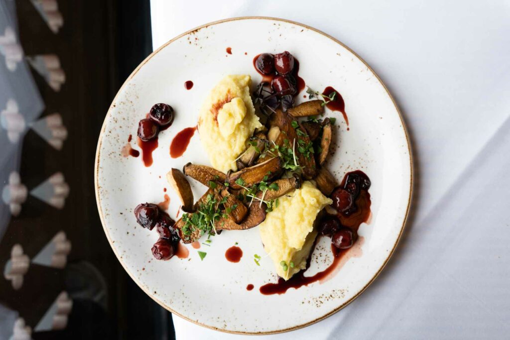 Dessertteller mit Eis, Früchten und Beerensauce auf hellem Geschirr.