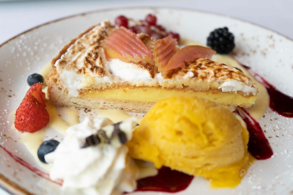 Dessert mit Eis, Früchten, Gebäck und cremiger Sauce auf einem Teller.