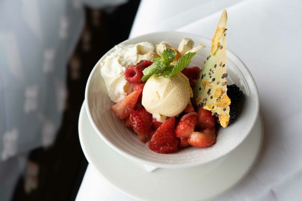 Dessert mit Sorbet, Beeren, Sahne und knuspriger Garnitur in einer Schale.