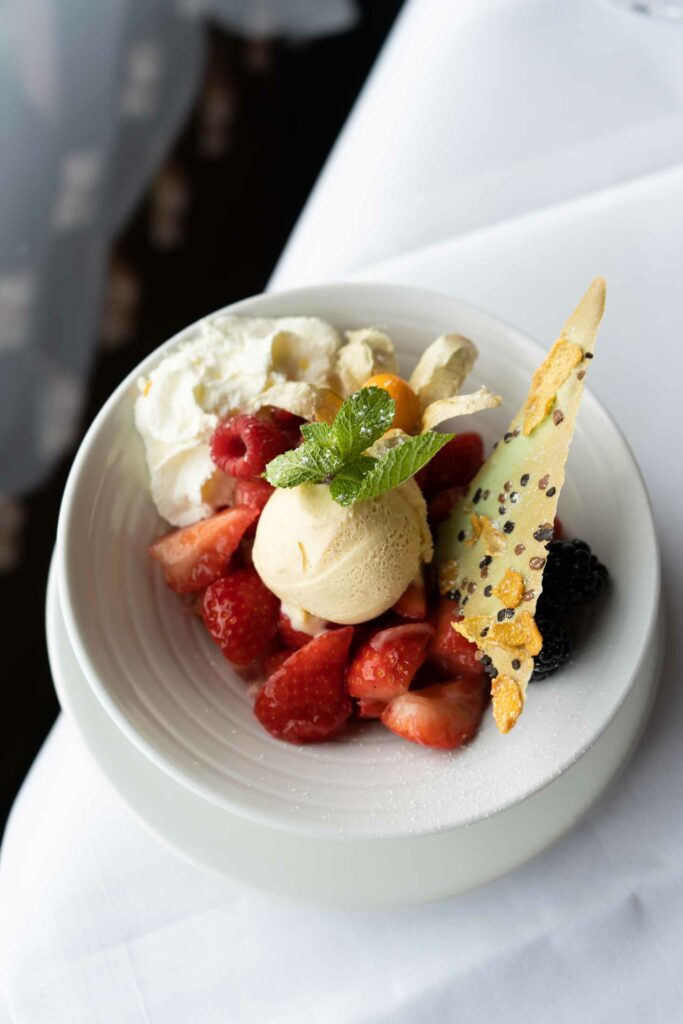 Dessert mit Sorbet, Beeren, Sahne und knuspriger Garnitur in einer Schale.