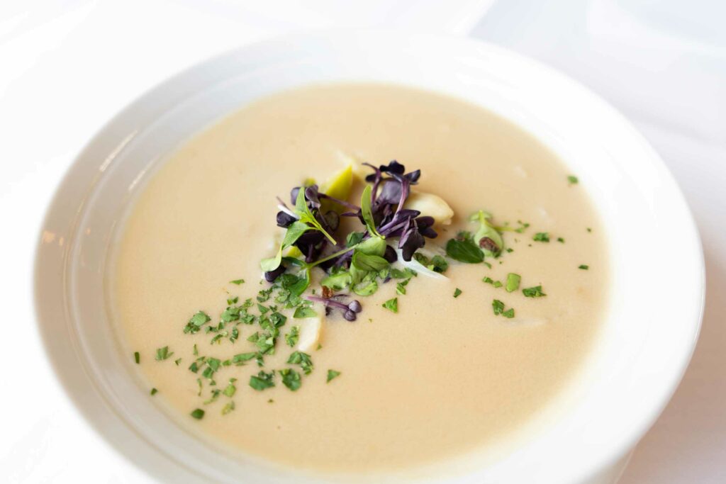 Helle Cremesuppe mit Kräutern und Blüten in einem tiefen Teller.