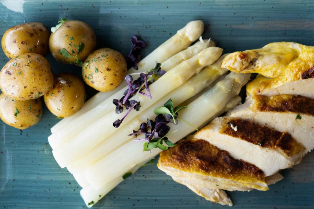 Spargelgericht mit Kartoffeln, Sauce und gebratenem Fisch auf einem rechteckigen Teller.