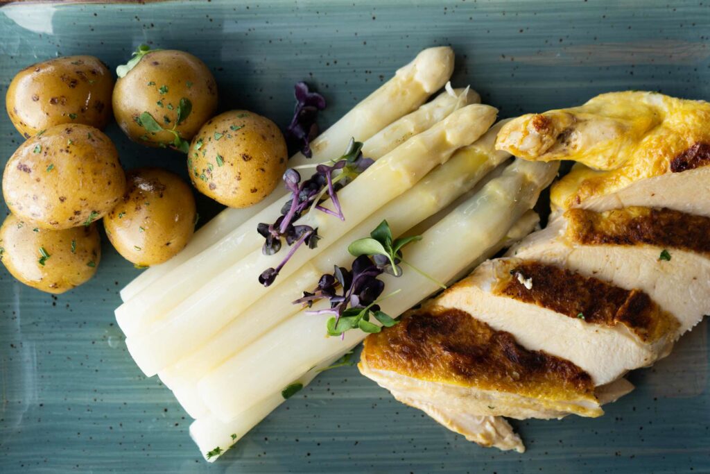 Spargelgericht mit Kartoffeln, Sauce und gebratenem Fisch auf einem rechteckigen Teller.