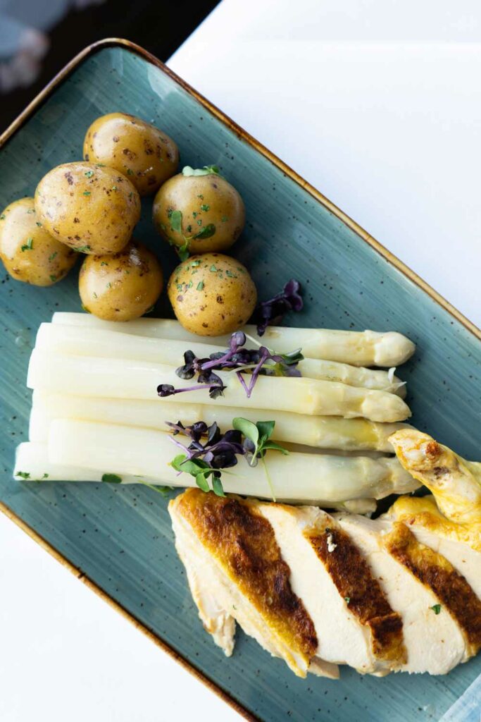 Spargelgericht mit Kartoffeln, Sauce und Kräutern auf einem rechteckigen Teller.