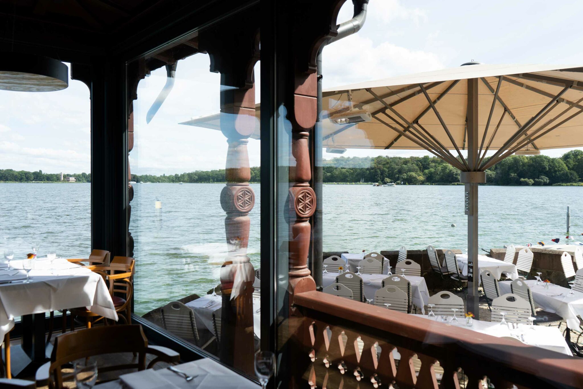 Überdachte Terrasse mit gedecktem Tisch, Holzgeländer und weitem Blick auf den See.