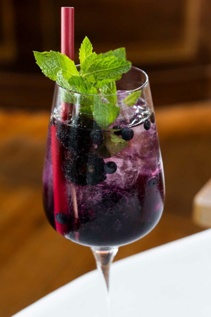 Dunkelroter Cocktail mit Beeren, Minze und Strohhalm in einem Weinglas.