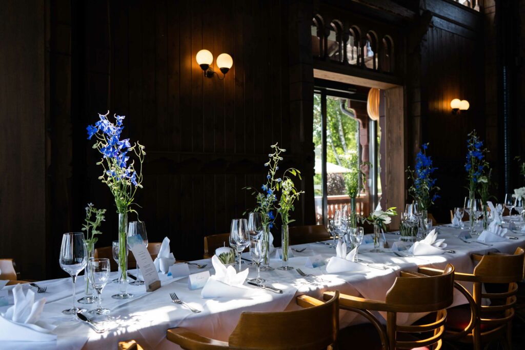Elegant gedeckte Tafel mit weißen Tischdecken, Gläsern und blauen Blumen im Restaurant.