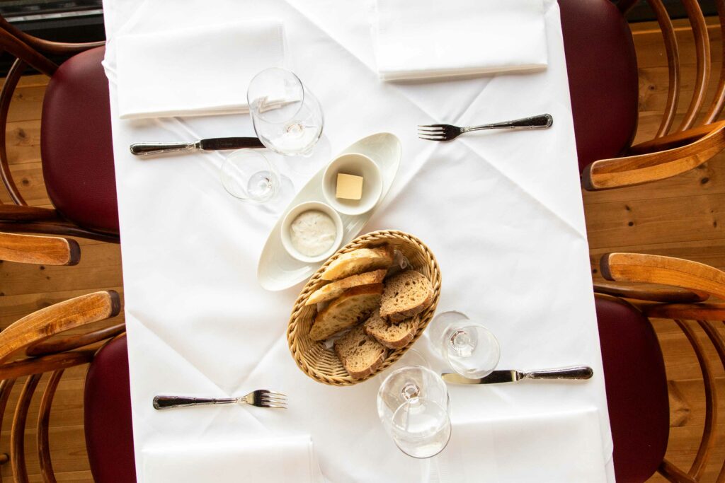 Weiß eingedeckter Restauranttisch mit Besteck, Gläsern und dekorativen Muscheln.