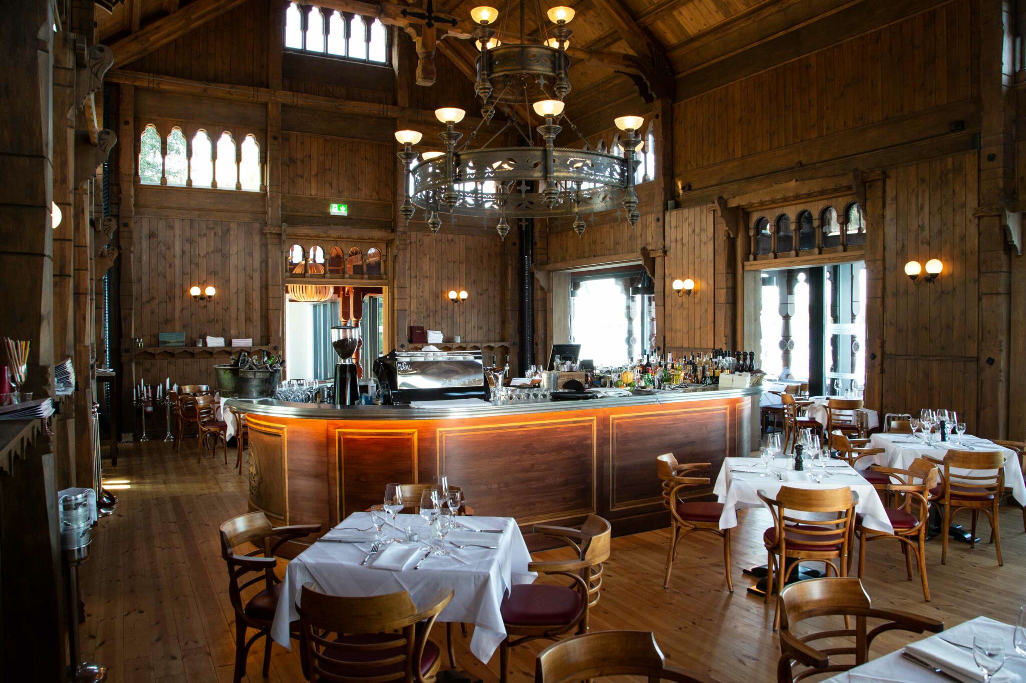 Restaurantinnenraum mit großer Holzbar, gedeckten Tischen und warmem Licht.