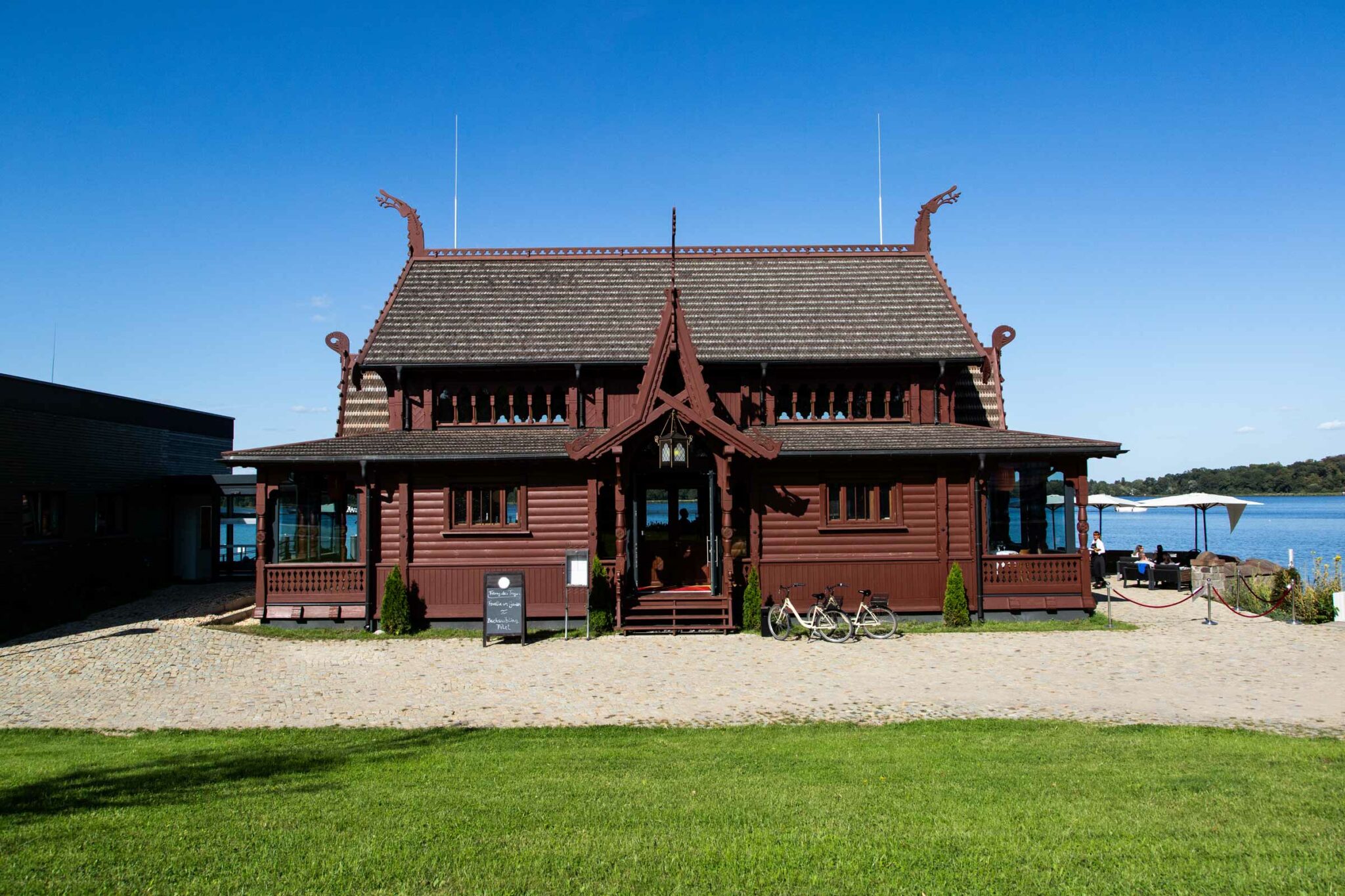 Kongsnaes Gebäude am See mit Holzfassade, Rasenfläche und blauem Himmel.