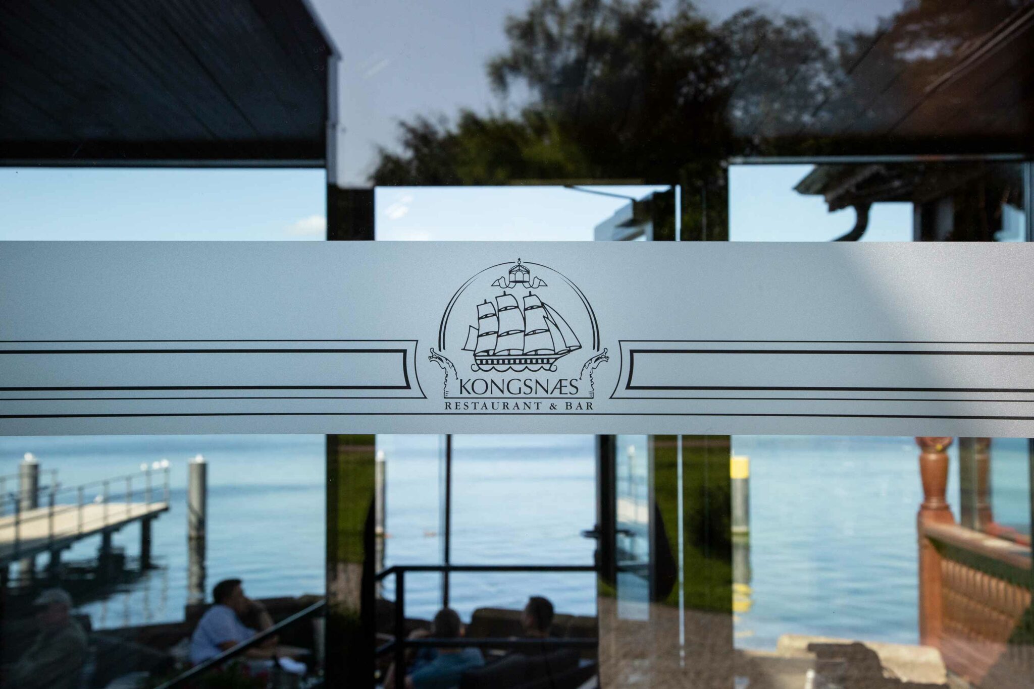 Blick von der Terrasse auf den See mit Logo-Grafik auf der Glasscheibe.