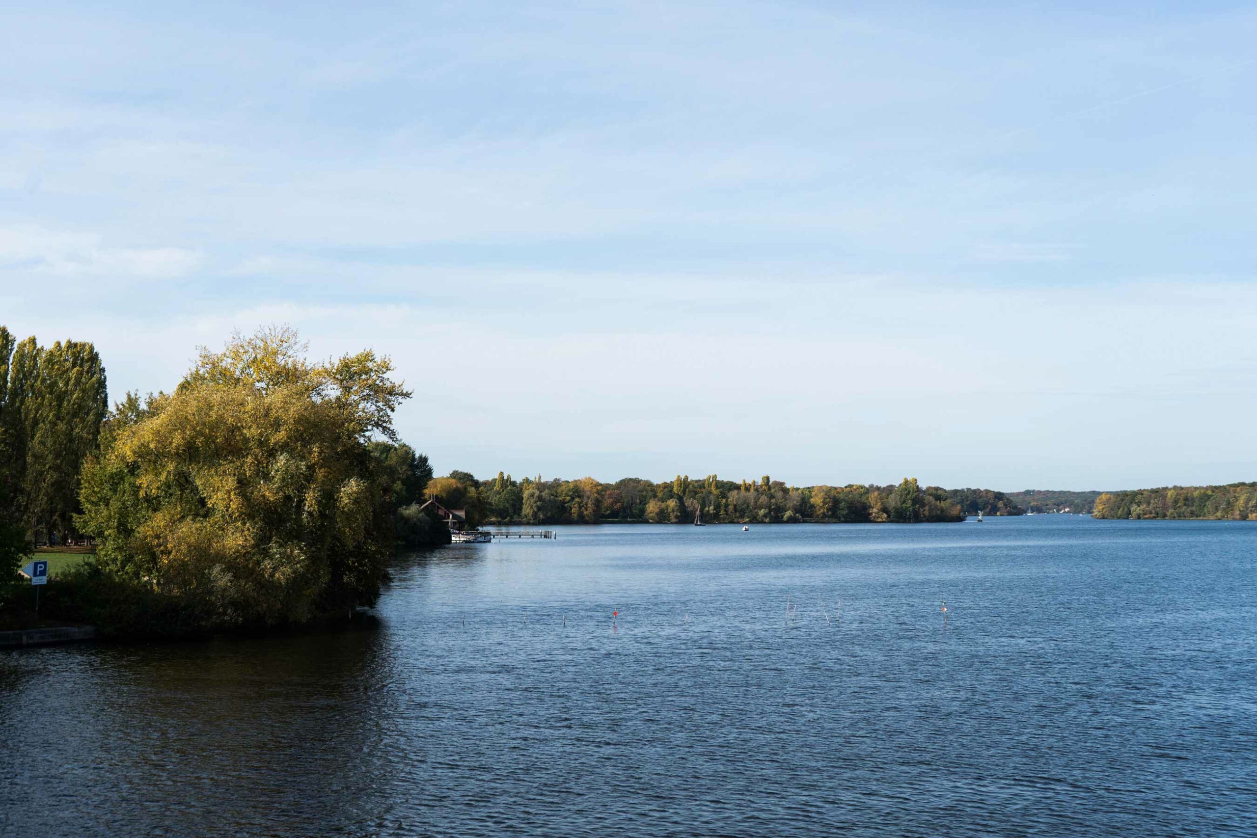 Weite Seelandschaft mit bewaldetem Ufer, ruhigem Wasser und hellem Himmel; mittig ist eine große Überschrift eingeblendet.