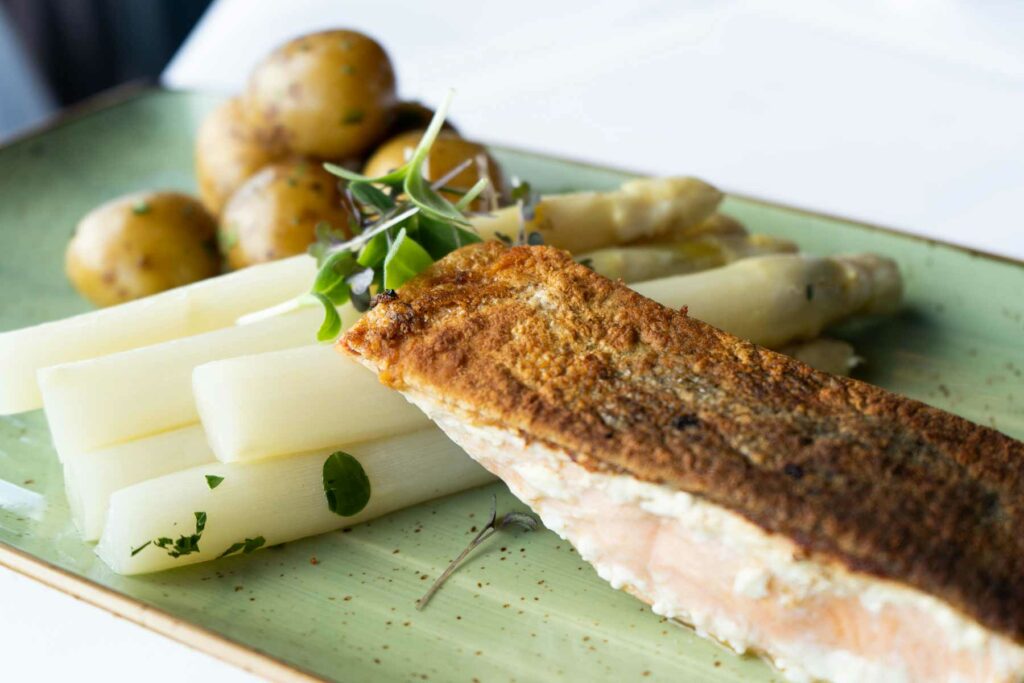 Fischfilet mit Spargel, Kartoffeln und Sauce auf einem rechteckigen Teller.
