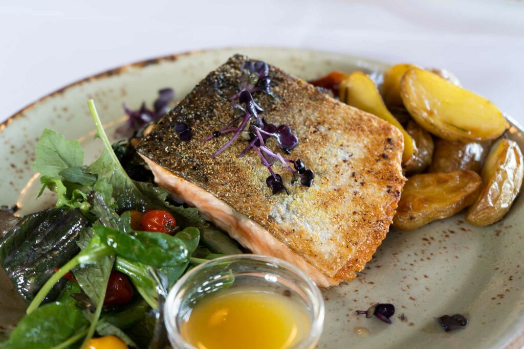Gebratenes Fischfilet mit Salat, Kartoffeln und Zitronensauce auf einem Teller.