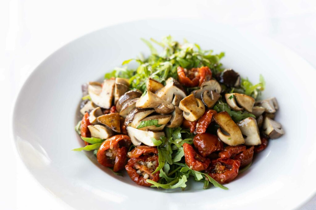 Bunter Salat mit Gemüse, Kräutern und Pilzen in einem weißen Teller.