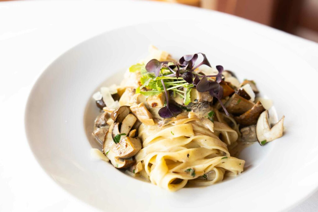 Teller mit Tagliatelle, Pilzen und Kräutern als angerichtetes Pastagericht.