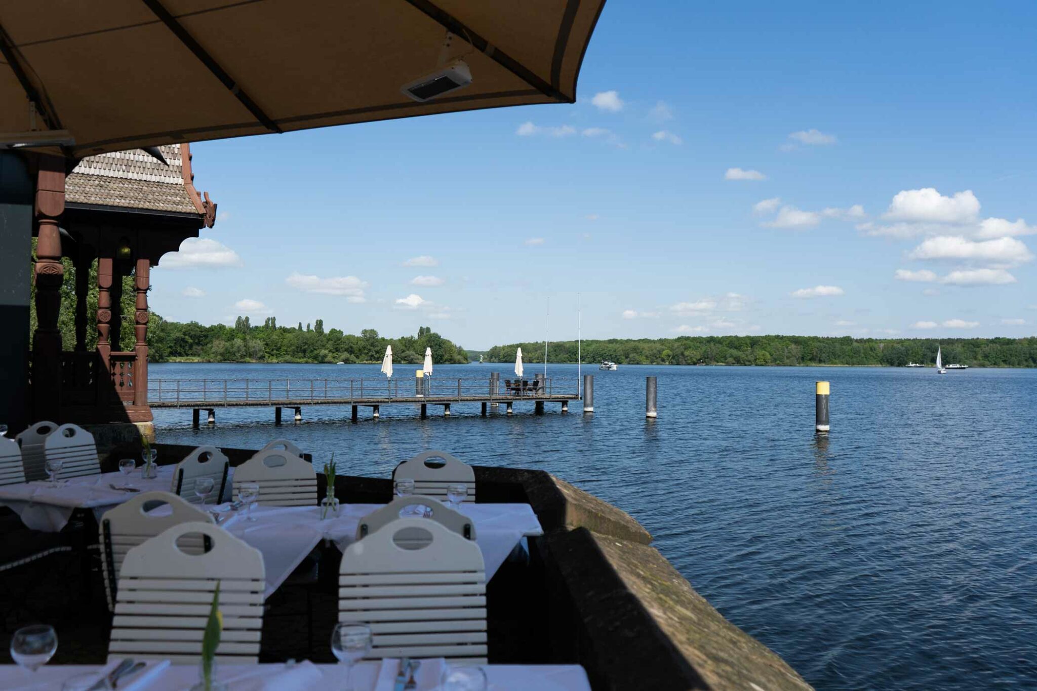 Seeterrasse mit gedeckten Tischen, Sonnenschirm und weitem Blick über das Wasser.