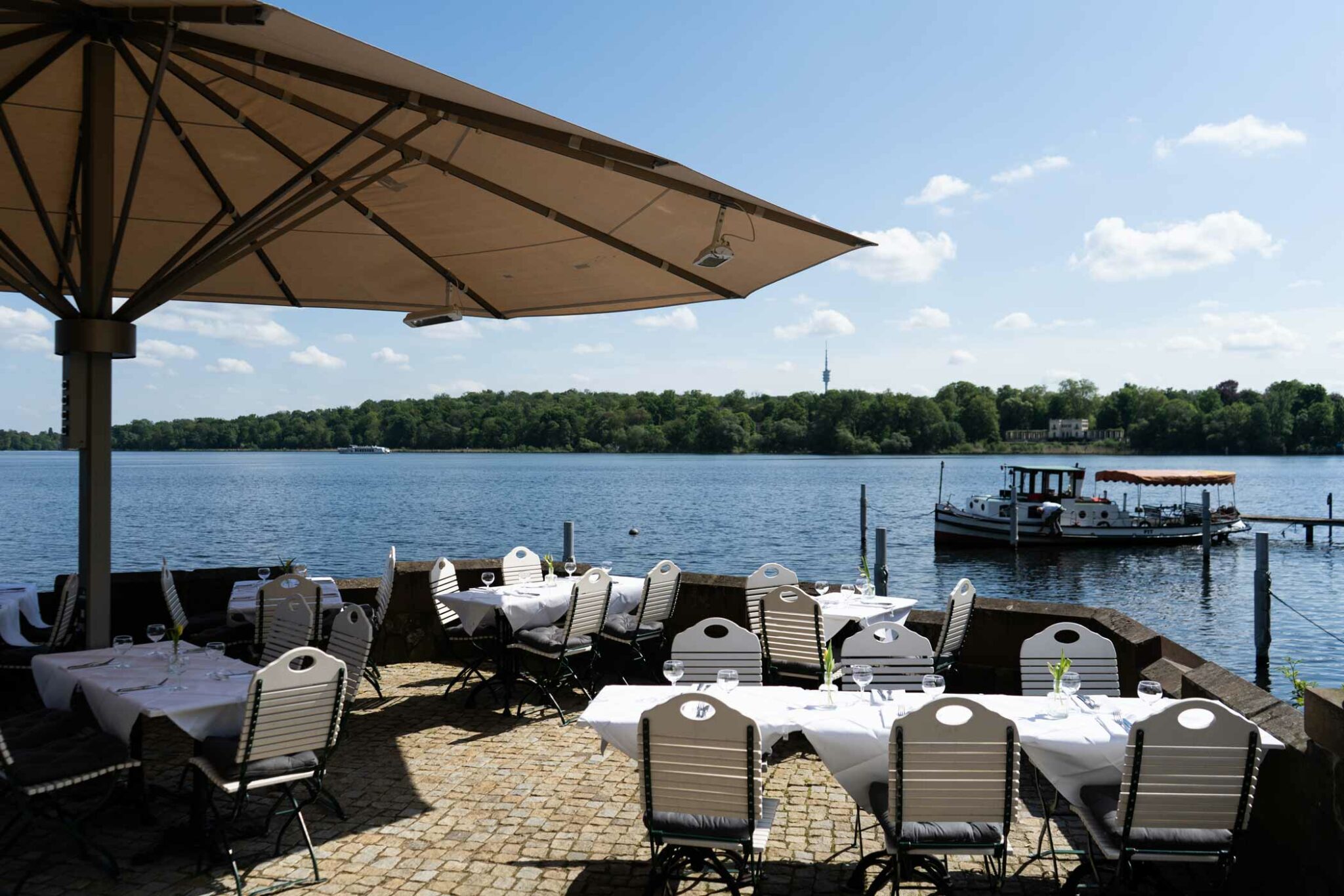 Außenterrasse mit weiß gedeckten Tischen, großen Sonnenschirmen und direktem Blick auf den See.