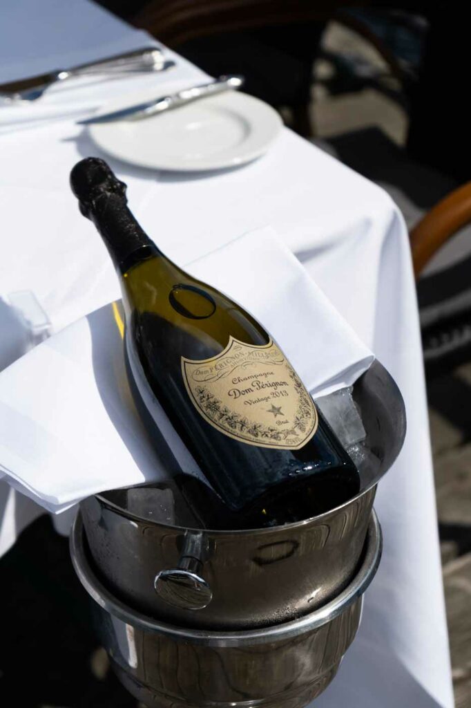 Champagnerflasche in einem silbernen Eiskübel auf einem weiß gedeckten Tisch im Außenbereich.