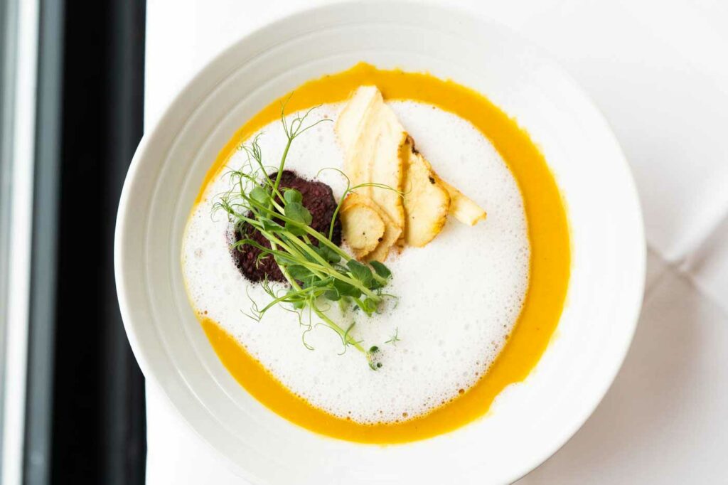 Cremige Suppe mit Kräutern und Garnitur in einem weißen Teller.