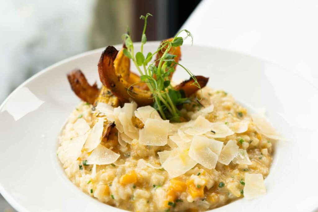 Cremiges Risotto mit gebratenem Gemüse, Kräutern und dekorativer Garnitur auf einem hellen Teller.