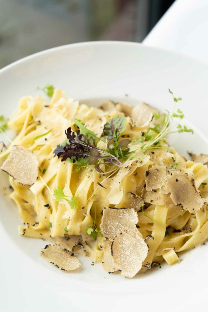 Pasta mit heller Sauce, Pilzen und Kräutern in einem weißen Teller.