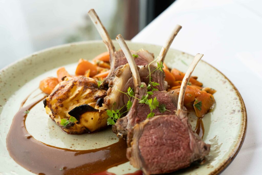 Fein angerichtetes Fleischgericht mit Gemüse, Sauce und Kräutern auf einem Teller.