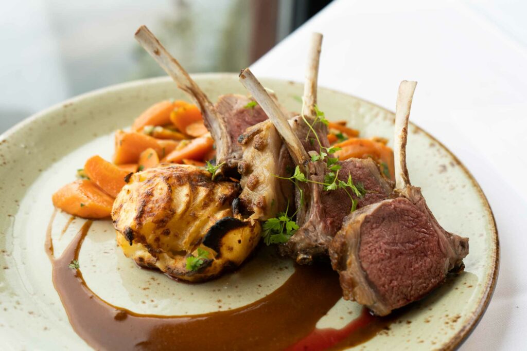 Fleischgericht mit Gemüse, Sauce und Kräutern auf einem großen Teller.