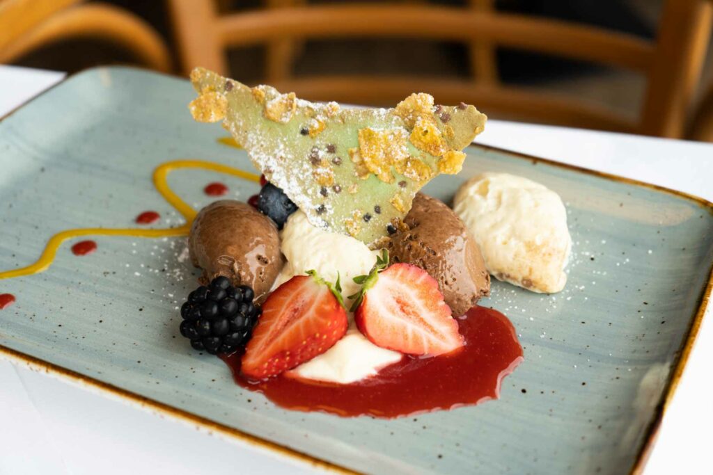 Dessert auf rechteckigem Teller mit Erdbeeren, Creme und Schokoladendekor.