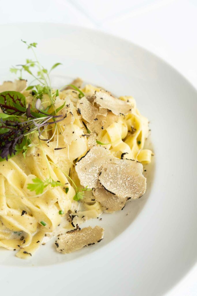 Pasta mit heller Sauce, Pilzen und frischen Kräutern in einem tiefen Teller.