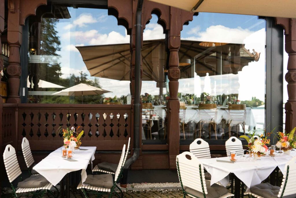 Überdachte Terrasse mit gedeckten Tischen, Holzsäulen und Blick auf den See.