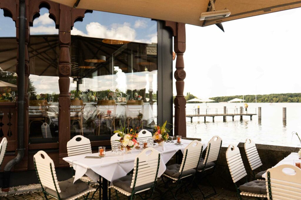 Terrasse am Wasser mit gedeckten Tischen, Sonnenschirm und Seeblick.