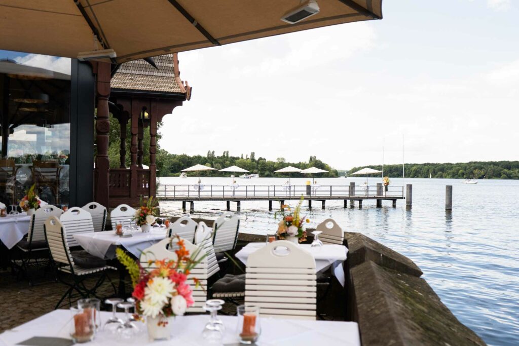 Restaurantbereich mit gedeckten Tischen, Blumen und Blick auf eine sonnige Terrasse.