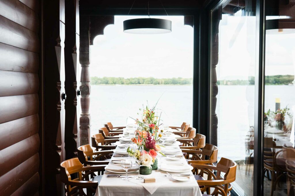 Lange festlich gedeckte Tafel im Restaurant mit großen Fenstern und Seeblick.