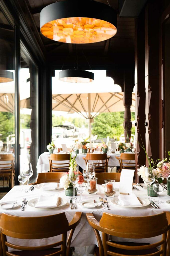 Restaurantbereich mit gedeckten Tischen, Blumen und Blick auf die Außenterrasse.