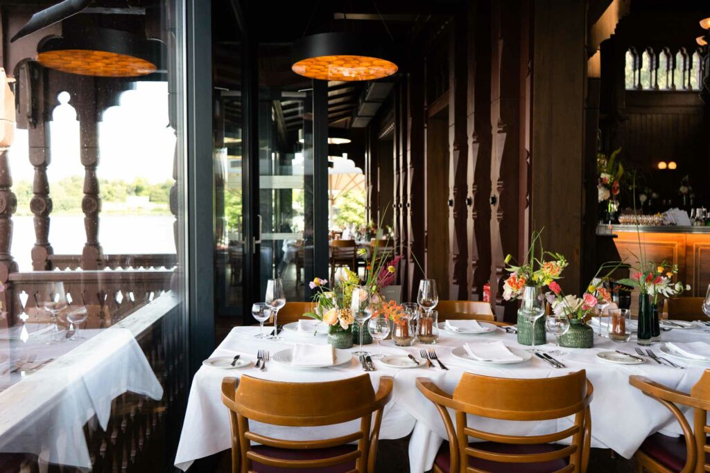 Restaurantinnenraum mit gedeckten Tischen, Holzmöbeln und großen Fensterfronten.