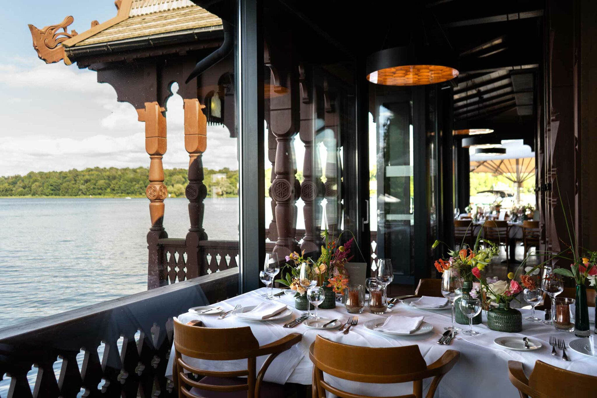Restaurantterrasse mit weiß gedeckten Tischen, Blumen und direktem Blick auf den See.