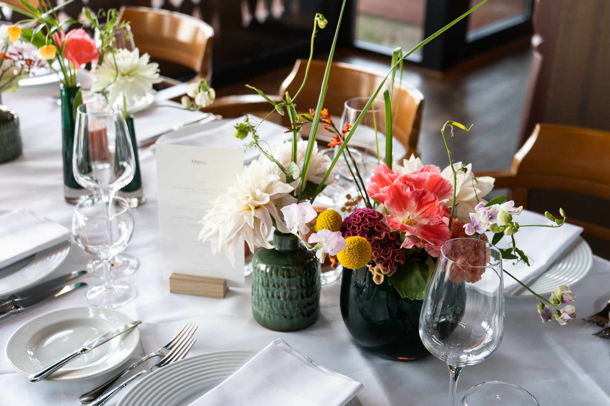 Nahaufnahme einer festlich gedeckten Tafel mit Blumenvasen, Gläsern und weißen Servietten.