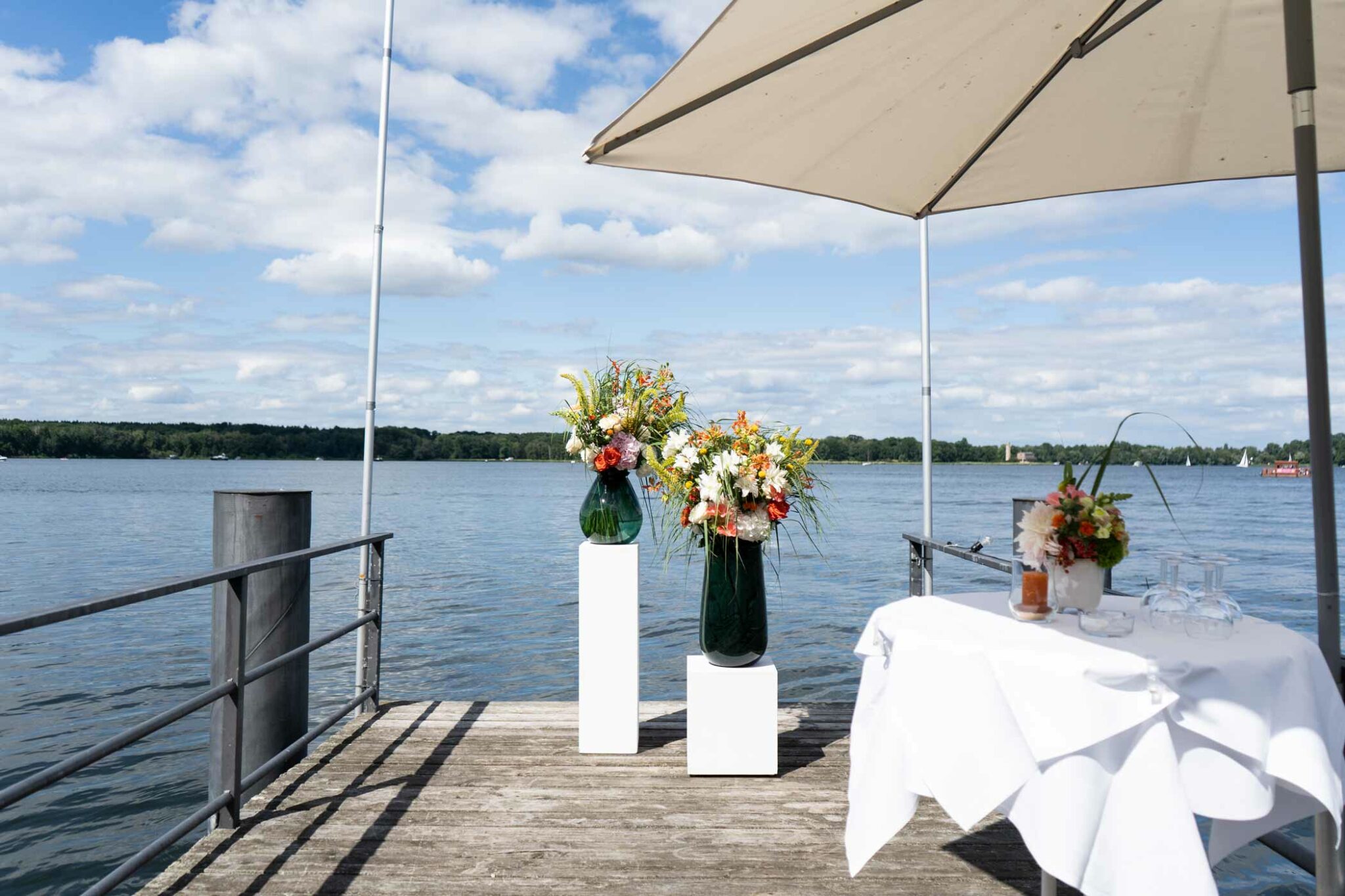 Festlich geschmückter Terrassentisch mit Blumen und Sonnenschirm direkt am Wasser.