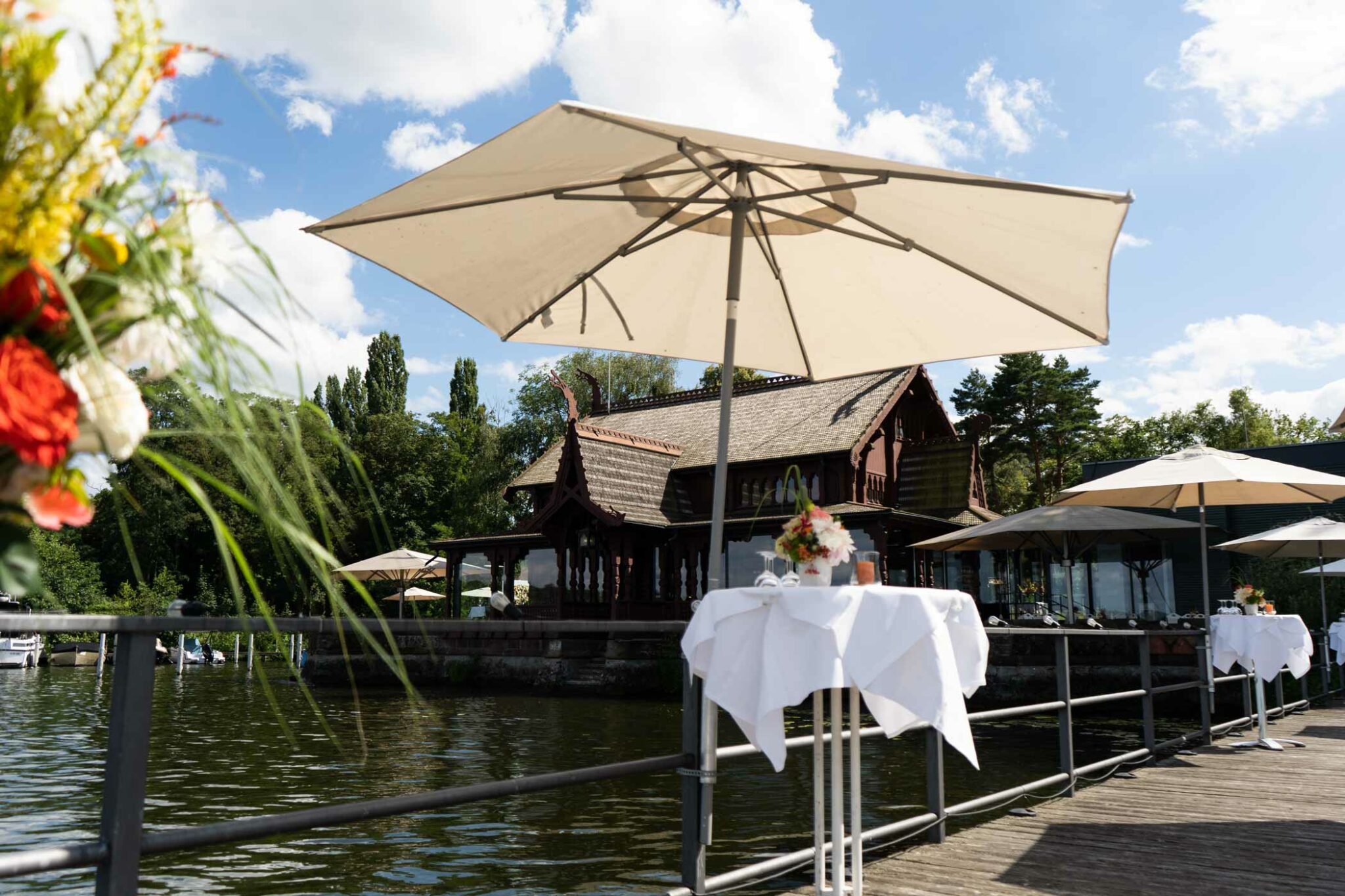 Terrasse am See mit Sonnenschirm, gedeckten Tischen und Uferblick.