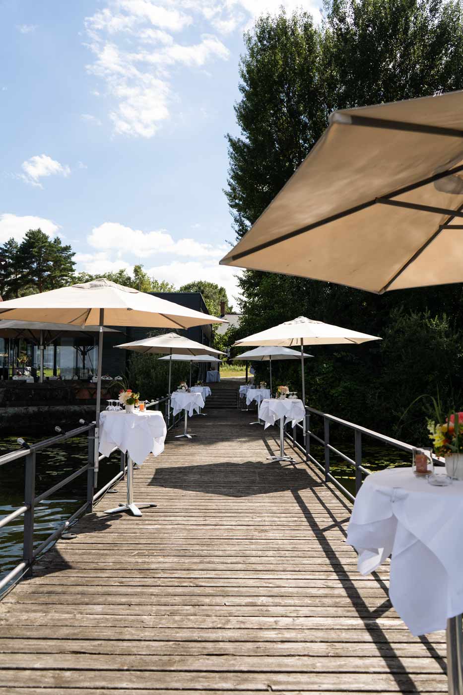 Gedeckte Tische mit Sonnenschirmen auf Seeterrasse.