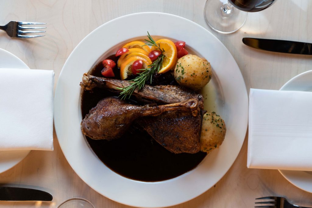 Gänsegericht mit Kartoffeln, Gemüse und dunkler Sauce auf einem weiß gedeckten Tisch.